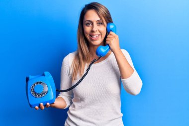 Kaliteli telefon tutan genç ve güzel bir kadın pozitif ve mutlu görünüyor. Kendine güvenen bir gülümsemeyle ayakta duruyor ve dişlerini gösteriyor. 