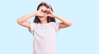 Sevimli İspanyol çocuk. Günlük beyaz tişört giyiyor. Kalp şeklinde, el ve parmaklarıyla gülümsüyor. 