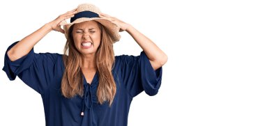Orta yaşlı İspanyol kadın yaz şapkası takıyor. Baş ağrısı çekiyor. Acı ve migren yüzünden çaresiz ve stresli. Eller başının üstünde.. 