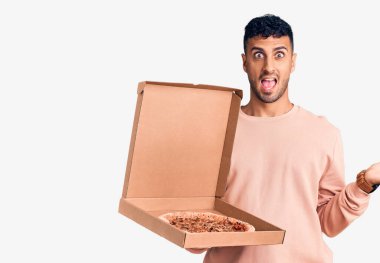 İspanyol asıllı genç adam elinde pizza kutusuyla zaferi kutluyor mutlu bir gülümseme ve ellerini kaldırarak kazanan bir ifadeyle. 