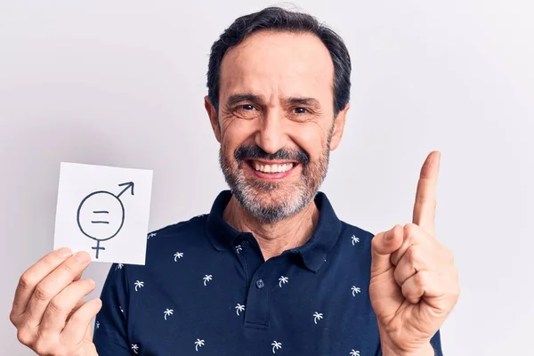 Middle age man asking for sex discrimination holding paper with gender equality message smiling with an idea or question pointing finger with happy face, number one