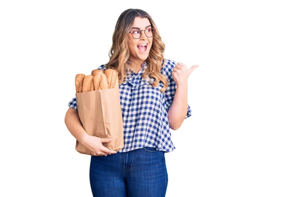 Joven Mujer Caucásica Sosteniendo Bolsa Papel Con Pan Apuntando Pulgar —  Fotos de Stock