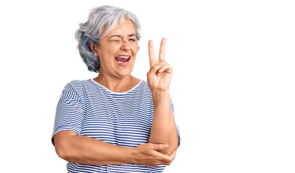 一位白发苍苍的老妇人 穿着随意的条纹衣服 满脸喜色地微笑着 在镜头前眨眼示意胜利 第二点 — 图库照片