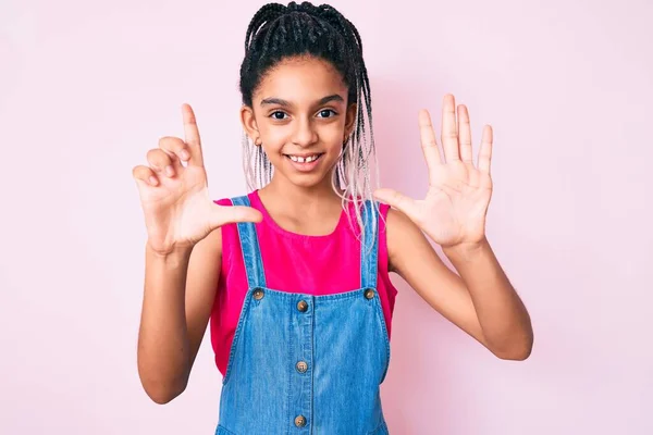 若いですアフリカ系アメリカ人の女の子子供とともにBraids身に着けていますカジュアル服上のピンクの背景表示と指摘指番号7ながら笑顔自信と幸せ — ストック写真