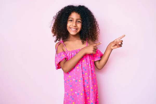 アフリカ系アメリカ人の子供で カジュアルなドレスを着て笑顔とカメラを見て2本の手と指で側面を指している — ストック写真