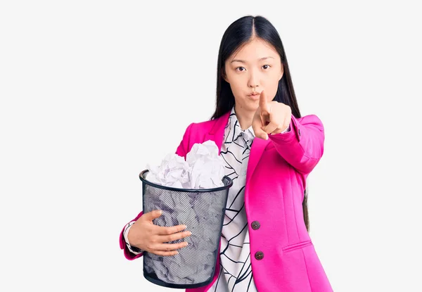 年轻美丽的中国女人拿着纸盒 满满是皱巴巴的纸盒 手指着相机 对着你 摆出一副严肃而自信的姿势 — 图库照片