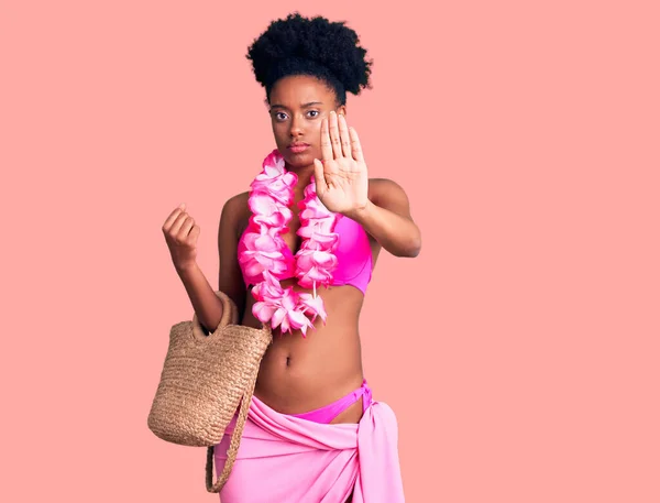 Young african american woman wearing bikini and hawaiian lei with open hand doing stop sign with serious and confident expression, defense gesture