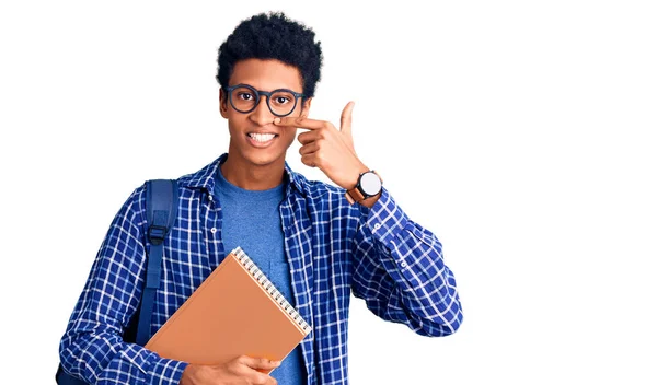 若いアフリカ系アメリカ人の男性は学生のバックパックを手指で顔や鼻を指して本を保持着て 陽気に笑顔 美の概念 — ストック写真