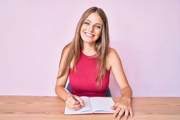 Jovem Caucasiana Escrevendo Caderno Sentado Mesa Olhando Positivo Feliz Sorrindo — Fotografia de Stock