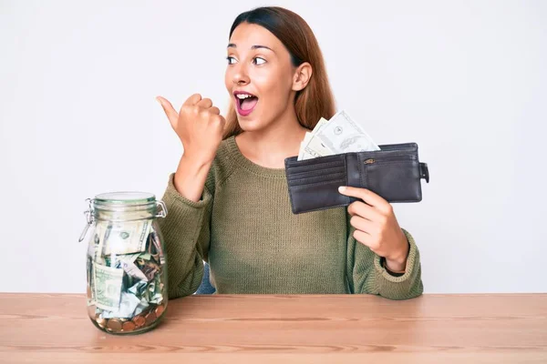 Young Brunette Woman Savings Jar Wallet Dollars Pointing Thumb Side — Stock Photo, Image