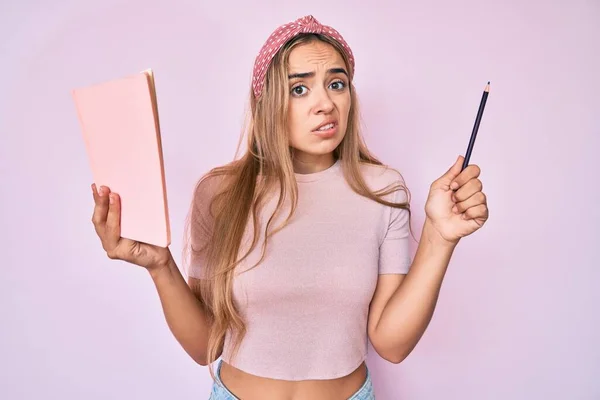 Młoda Piękna Blondynka Trzymająca Książkę Ołówek Bez Pojęcia Zdezorientowana Ekspresja — Zdjęcie stockowe