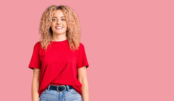 Young blonde woman with curly hair wearing casual red tshirt with a happy and cool smile on face. lucky person.