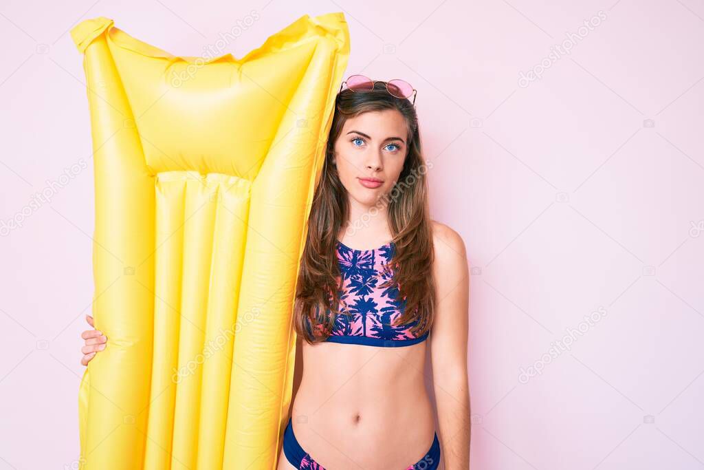 Beautiful young caucasian woman wearing bikini and holding summer matress float thinking attitude and sober expression looking self confident 