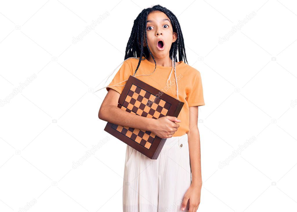 Cute african american girl holding chess scared and amazed with open mouth for surprise, disbelief face 