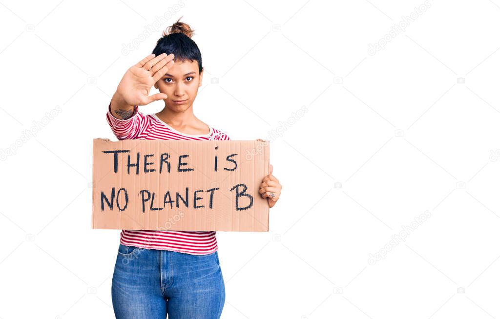 Young woman holding there is no planet b banner with open hand doing stop sign with serious and confident expression, defense gesture 