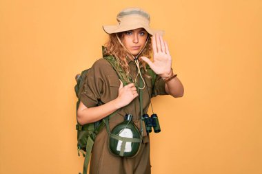 Mavi gözlü, sırt çantalı ve su kantinli genç sarışın kaşif avucuyla şarkı söylemeyi kesiyor. Yüzünde olumsuz ve ciddi bir jest olan uyarı ifadesi.