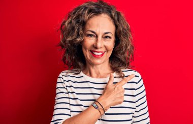 Orta yaşlı, esmer, çizgili tişört giyen, kırmızı arka planda duran güzel bir kadın.