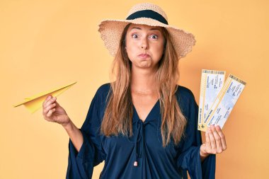 Orta yaşlı İspanyol kadın yaz şapkası takıyor elinde biniş kartı ve kağıt uçak komik suratlı yanakları şişiriyor. Ağzı havayla şişer, havayı yakalar.. 