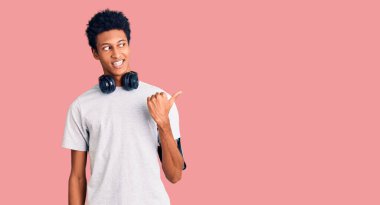 Genç Afro-Amerikalı adam spor kıyafetleri giyiyor ve kulaklık takıyor. Gülümsüyor, gülümsüyor ve baş parmağıyla yan tarafa bakıyor.. 