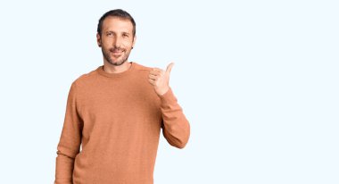 Genç, yakışıklı, sıradan kıyafetler giyen, gülen yüzlü, gülümseyen ve baş parmağıyla yan tarafı gösteren bir adam.. 