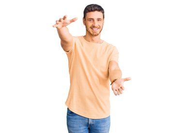 SarıImak için kollarını açıp kameraya gülümseyen, sarı tişörtlü, ayılı yakışıklı bir genç. Mutluluğu kucaklayan neşeli bir ifade.. 