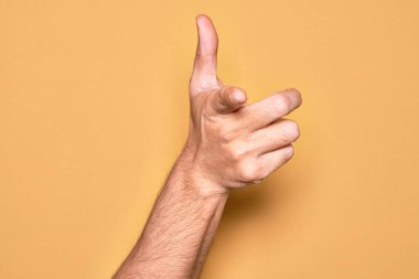 İzole edilmiş sarı arka plan üzerinde parmaklarını gösteren beyaz bir genç adamın eli kamerayı işaret ediyor ve yönü gösteriyor.