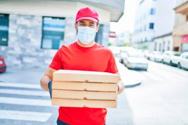 Üniforma giyen ve koronavirüs koruma maskesi takan genç teslimatçı. Kasaba caddesinde pizza kutularını teslim ediyorum..