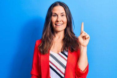 Genç, güzel, esmer, iş kadını. Mavi arka planda duran ceketli. Bir fikir veya soruyla gülümseyen.
