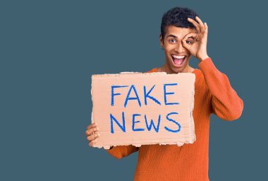 Genç Afrikalı Amerikalı adam elinde sahte haber afişi tutarken mutlu bir şekilde gülümsüyor. 