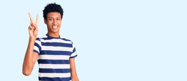 Genç Afro-Amerikalı günlük kıyafetler giymiş iki numarayı gösterip işaret ederken kendinden emin ve mutlu gülümsüyor.. 