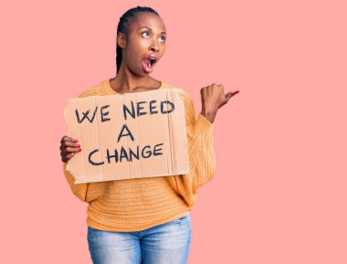 Genç Afro-Amerikalı kadın elinde bir değişim pankartı tutarken başparmağımızı kaldırıp gülümsüyoruz, ağzı açık bir şekilde. 