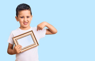 Küçük sevimli çocuk elinde boş bir çerçeve tutarak gülümseyen mutlu ve gururlu birini işaret ediyor. 
