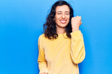 Gündelik giysiler giymiş genç, güzel İspanyol bir kadın. Başarının şaşkınlığını ve şaşkınlığını kutluyor. Kolları havada, gözleri kapalı. 