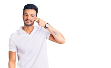 Gündelik giysiler giyen genç, yakışıklı İspanyol adam, el parmağı ve burunla işaret ediyor, neşeli bir şekilde gülümsüyor. güzellik konsepti 