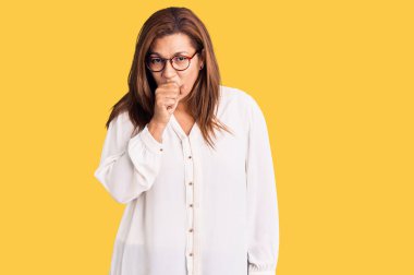 Orta yaşlı Latin bir kadın günlük kıyafetler ve gözlük takıyor kendini iyi hissetmiyor ve soğuk algınlığı veya bronşitin belirtisi olarak öksürüyor. sağlık hizmeti kavramı. 