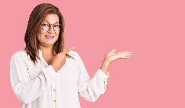 Orta yaşlı Latin kadın gündelik kıyafet ve gözlük takıyor kameraya hayret ediyor ve gülümsüyor.. 