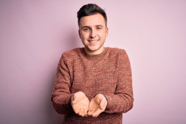 Pembe izole edilmiş arka plan üzerine sıradan bir kazak giyen yakışıklı beyaz adam avuçlarını birbirine uzatarak gülümsüyor ya da jest yapıyor. Tutun ve koruyun