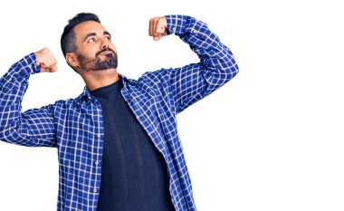 Sıradan kıyafetler giyen genç İspanyol adam gururla gülümseyen kol kaslarını gösteriyor. fitness konsepti. 