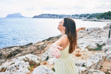 Genç ve güzel bir kadın, kumsalda kolları açık nefes alıyor.