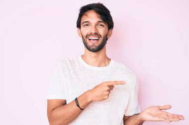 Beyaz tişört giyen yakışıklı İspanyol adam kameraya hayret ediyor ve gülümsüyor. Elle ve parmakla işaret ediyor.. 