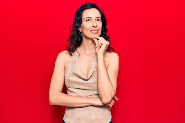 Gündelik giysiler giyen genç, İspanyol bir kadın kameraya kollarını kavuşturup, çenesine dokunarak gülümsüyor. Olumlu düşünmek. 