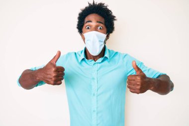 Yakışıklı Afro saçlı, tıbbi maske takan, şaşırmış ve şaşırmış bir ifadeyle korku ve heyecan dolu bir yüzü olan Afro-Amerikan erkeği.. 