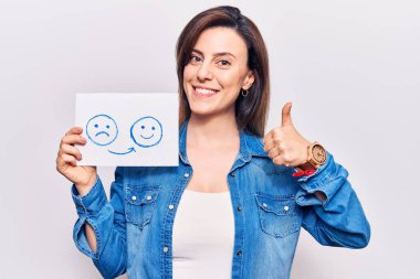 Genç, güzel bir kadın, elinde mutlu duygu kağıdıyla gülümsüyor, mutlu ve olumlu gülümsüyor, başparmağıyla mükemmel ve onay işareti yapıyor. 