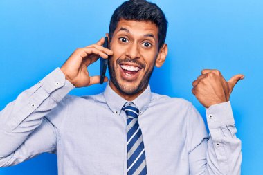 Genç latin adam akıllı telefondan konuşuyor başparmağını kaldırıyor ve ağzı açık gülümsüyor. 