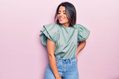 Genç ve güzel esmer kadın mutlu ve kendinden emin gülümsüyor. İzole edilmiş pembe arka planda yüzünde bir gülümsemeyle duruyorum.