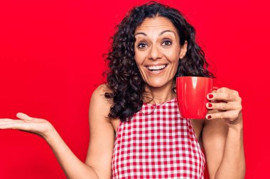 Orta yaşlı güzel bir kadın bir kupa kahve içip başarıyı mutlu bir gülümsemeyle kutluyor ve kazanan el kaldırarak ifade ediyor. 