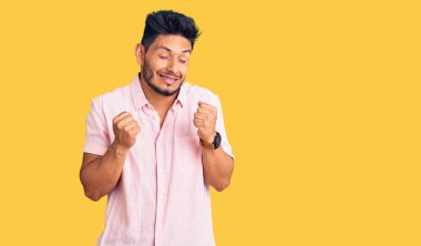 Yakışıklı Latin Amerikalı sıradan bir yaz gömleği giyen başarılı olmak için heyecanlanan kolları havada ve gözleri kapalı zaferi kutlayan genç adam. Kazanan konsept. 