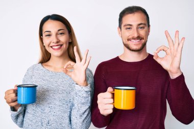 Güzel bir çift ellerinde kahve tutuyorlar parmaklarıyla işaret veriyorlar, gülümsüyorlar mükemmel bir sembol. 