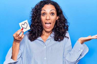 Orta yaşlı güzel bir kadın elinde kalp ile başarıyı mutlu bir gülümsemeyle ve kazanan bir ifadeyle kutluyor. 