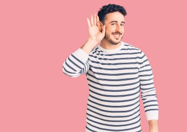 Gündelik kıyafetler giyen, ağzı kulaklarında gülümseyen genç İspanyol bir adam dedikoduları ve dedikoduları dinliyor. Sağırlık kavramı. 